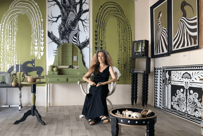 Une femme assise dans un fauteuil dans une galerie d'art, entourée de peintures et de décorations murales aux motifs abstraits en noir et vert.